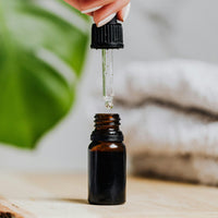 Hand using a dropper to add  diffuser oil to an amber bottle on a wooden surface with a blurred natural background