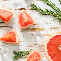 Slices of pink grapefruit with rosemary on a light wooden surface
