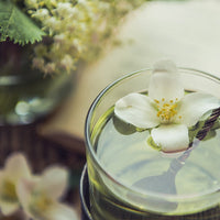 Glass of green tea with jasmine flowers on a blurred natural background